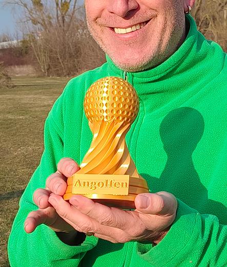 Ich stehe auf unserem Crossgolf Platz und halte einen goldigen kleinen Pokal vor meiner Brust.
Ich selber trage eine knallig grüne Jacke und lächel in die Sonne, die mir ins Gesicht scheint