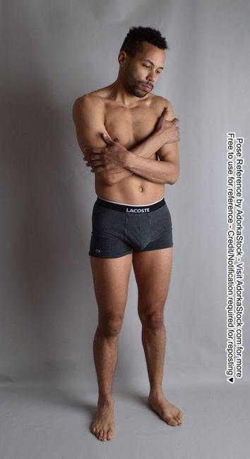 A photo of a latino man in his underwear, arms loosely crossed over his chest, looking off dejectedly.