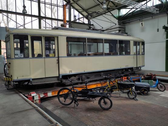 Mehrere verschiedene Lastenräder sind vor einer alten Straßenbahn aufgestellt. Der Innenraum lässt erkennen, dass es sich hier um ein ehemaliges Straßenbahndepot handelt