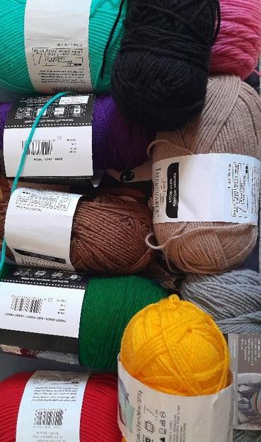 Several skeins of yarn in various colors. On the left side from top to bottom:Cyan, purple, brown, green, and red. On the right side from top to bottom: Black, pink, beige, gray, yellow.