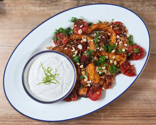 Das fertige Gericht wie beschrieben auf einer Servierplatte mit einer Schale mit Joghurt + Limettenzesten