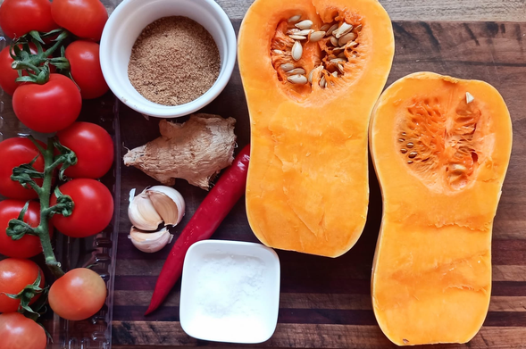 auf dem Tisch Tomaten, Knoblauch, Ingwer Mascovadozucker, 1 rote Chili, Salz und ein halbierter Butternusskürbis