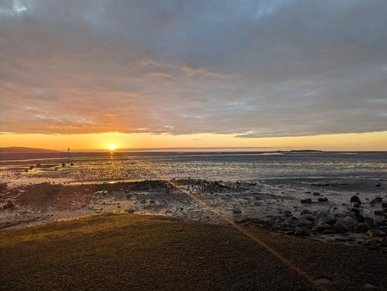 sun setting over an estuary. there tide is out. there are low islands and wind turbines visible in the distance