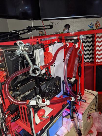 Photo of a red PC sitting on a table. The PC components are mostly red and black. It is cooled by a liquid cooling system pumping red fluid through clear tubing.