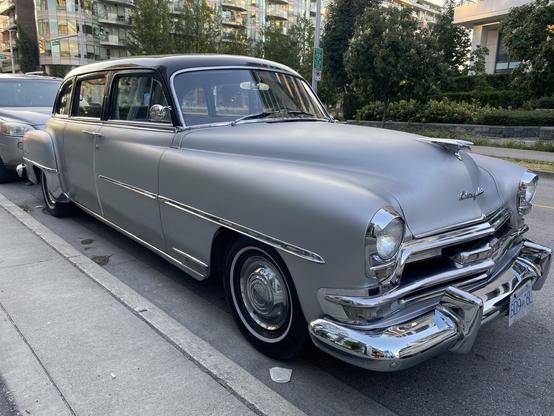 Very old car (possibly early-1950s), with a black roof and silvery-pearl body, seen in a three-quarter angle.