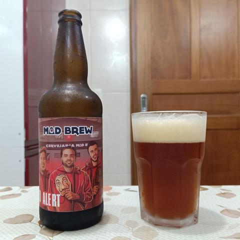 Garrafa de 600 ml da cerveja Mad Brew no lado esquerdo, copo com a cerveja servida no lado direito. É um líquido de cor cobre escuro com colarinho cremoso. O sabor é bastante carregado no malte (aka "docinha")