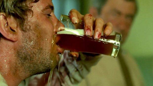 A still from the movie, "Wake in Fright" A sweaty man skulling a pint of beer with bloody knuckles