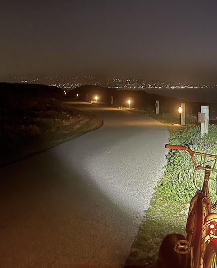 Low-to-ground post lights line the Monterey Bay coastal trail. A BMX is parked at right in foreground. In background are the lights of City of Monterey.