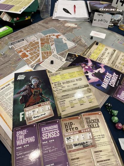 The City of Mist table during a break in play, with a map covered with character folios, clues, status cards, dice and notes.