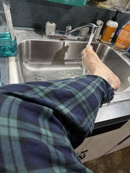 A toe attached to a foot attached to a leg being put in a sink under running water
