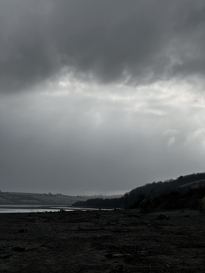 A dark, cloudy sky looms over a landscape with a body of water and hills in the distance, creating a moody atmosphere.