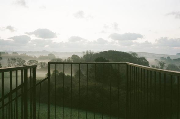 2025/062: Mist rises from the lush meadows along the River Dart before the sun, which will soon appear on the horizon, dispels it. A fenced-in view of the rolling Devon countryside.