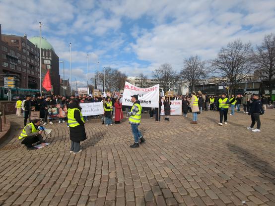 Demonstration von Jesidinnen und Jesiden für ihr Bleiberecht. Rote Flagge. Menschen mit Bannern "Retten Sie bitte unsere Kinder"
"Bleiberecht"

Menschen mit gelben Westen