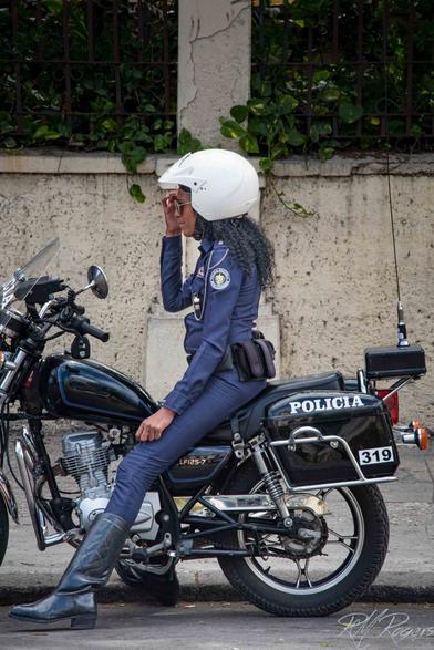Photograph of a Cuban motorcycle policewoman in uniform astride her bike.