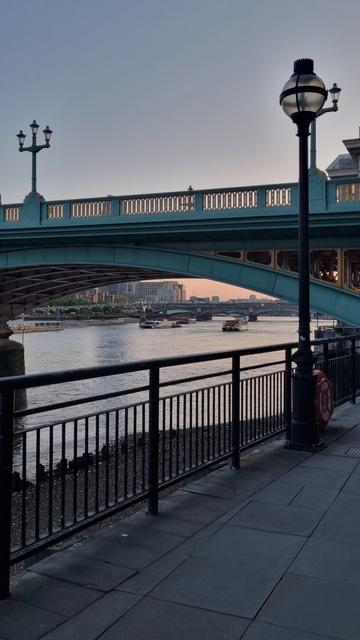 Scenery of the promenade next to Thames river. Bridge crossing  the river, light poles. Another bridge in he distance.
