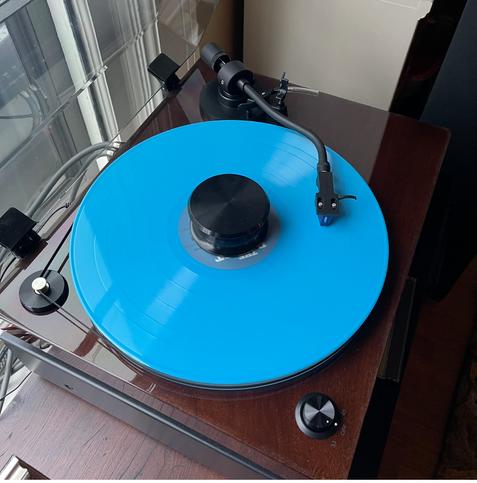 Bright blue vinyl record album on a half decent stereo turntable with faux walnut finish, curved aluminum tonearm with Ortofon Blue cartridge and exterior belt drive.
