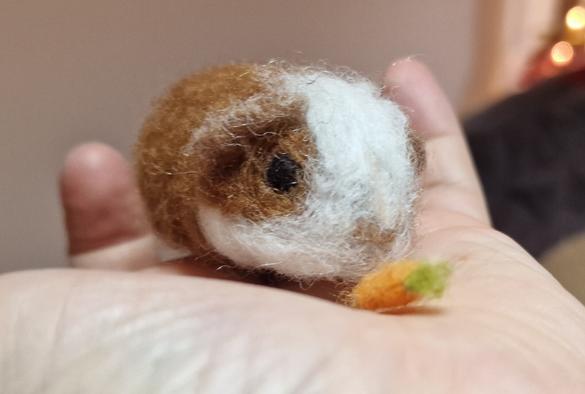 A brown and white guinea pig with carrot on my hand. Made of wool.