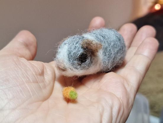 A grey guinea pig with carrot on my hand. Made of wool.