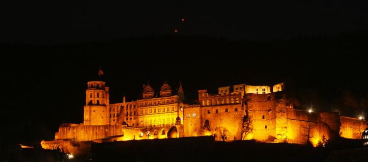 Eine Nachtaufnahme vom Heidelberger Schloß. Das Schloß wird durch Scheinwerfer orange beleuchtet.