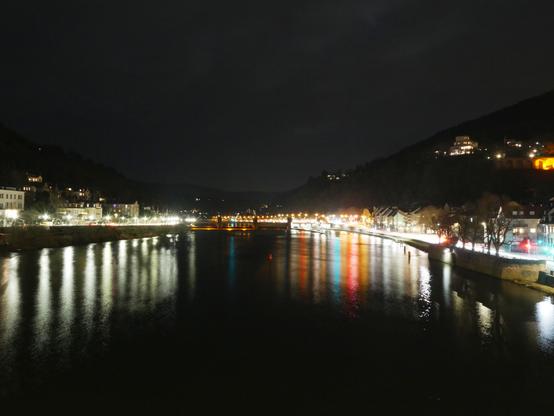 Eine Langzeitbelichtung vom Neckar in Heidelberg. Man seiht den Fluß, die beleuchteten Straßen rechts und LInks, die Gebäude, die die Berge hinauf gehen und weiter hinten eine weitere Brücke