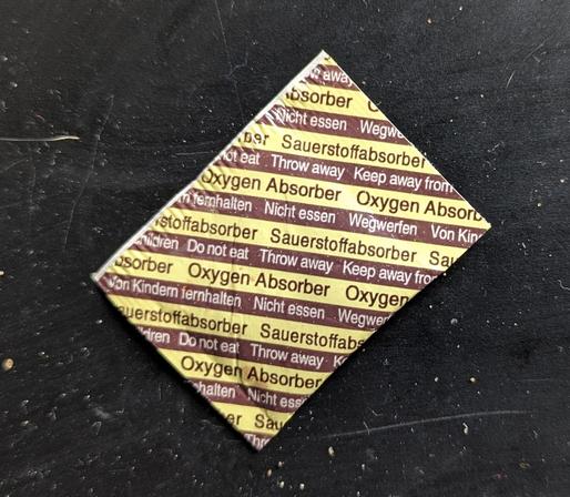 A small plastic sachet with "Oxygen Absorber" and "Do Not Eat" written on it in English and German.