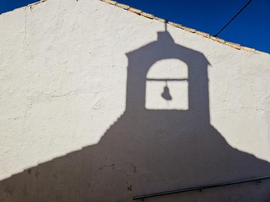 Shadow of a small church belltower on a whitewashed wall in bright sunshine