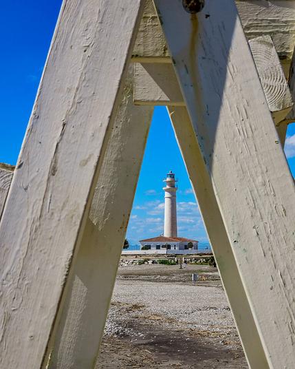 A white lighthouse visible in the distance through an A shaped whitewashed wooden structure