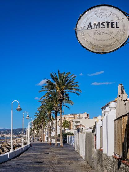 A faded oval Amstel sign above a seaside path