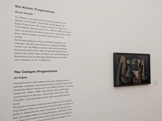 Links: Text auf Deutsch und Englisch an einer weißen Wand, rechts ein Ölgemälde