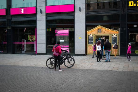 Eine Frau und Mädchen mit rosa Kleidungsstücken vor einem Telekom-Geschäft mit rosa Reklame.