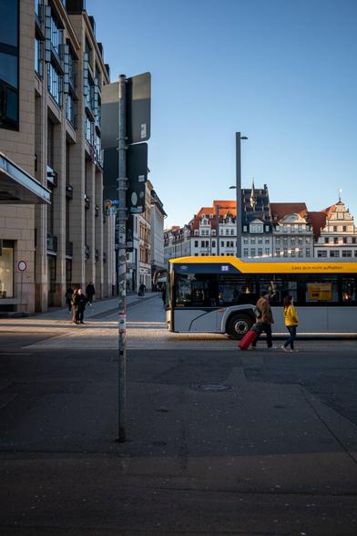 Eine Frau mit gelber Jacke vor einem Bus der LVB mit gelb abgesetzter Dachkante.