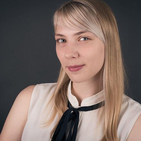 Portraitfoto einer jungen blonden Frau im weißer ärmelfreier Bluse mit schwarzer Schleife.