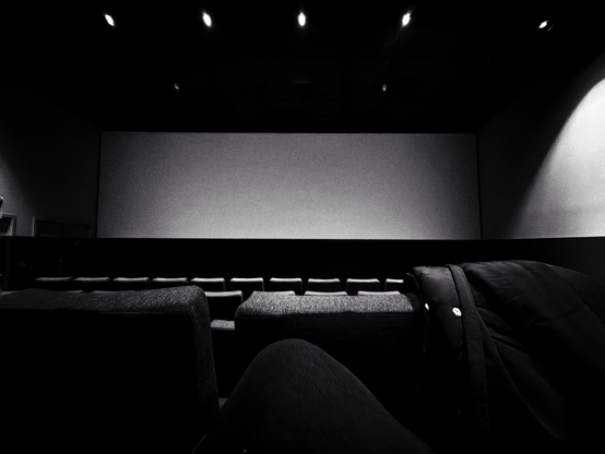 Empty cinema with a blank screen and rows of seats, with a coat hanging over them.