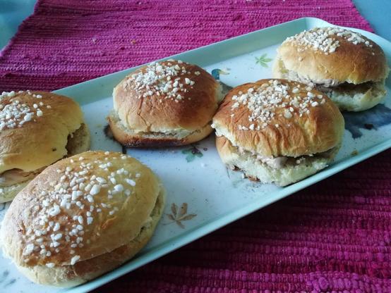 Muovitarjottimella on viisi pullaa, joiden välissä on suklaavaahtoa ja päällä raesokeria. Tarjotin on sinisen pöydän ja purppuranpunaisen poppanan päällä.