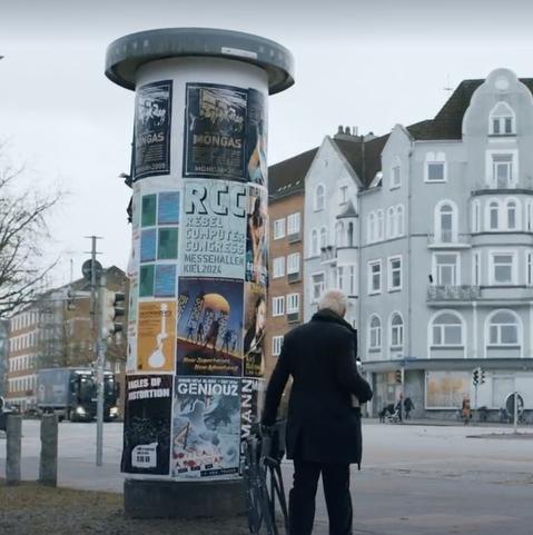 Ein Ausschnitt aus dem Kieler Tatort. Auf einer Litfasssäule neben anderen Eventplakaten eines für den Rebel Computer Congress in Kiel.