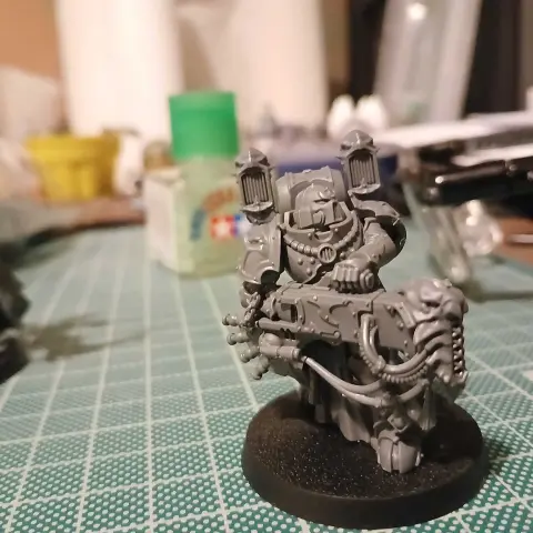 A Noise Marine for Warhammer 40,000. His helmet, right shoulder pad, and both sides of his backpack include speaker systems. In both hands he carries a bulky energy weapon called a sonic weapon, the front of which is stylised to look like a demonic face.