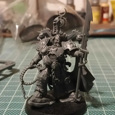 A Lord Exultant model for Warhammer 40,000, armed with a "Phoenix pattern" power spear and a rapture lash (effectively a hooked bullwhip). He stands imperiously in a pair of rocks with a stern, scarred face, and a cape billows dramatically behind him.