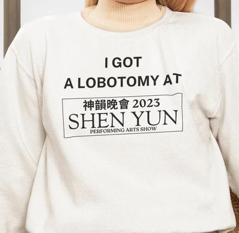A person wearing a cream-colored sweatshirt with bold black text that reads:

“I GOT A LOBOTOMY AT”

Below this, there is a rectangular logo mimicking promotional materials for Shen Yun, a well-known performing arts show. The logo includes Chinese characters, the year “2023,” and the words “SHEN YUN PERFORMING ARTS SHOW.”
