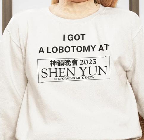 A person wearing a cream-colored sweatshirt with bold black text that reads:

“I GOT A LOBOTOMY AT”

Below this, there is a rectangular logo mimicking promotional materials for Shen Yun, a well-known performing arts show. The logo includes Chinese characters, the year “2023,” and the words “SHEN YUN PERFORMING ARTS SHOW.”