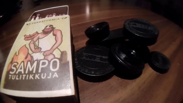 A matchbox and smartphone camera accessory lenses on a table. A wide angle shot.