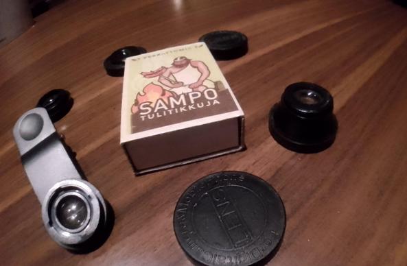 A matchbox and some smartphone camera accessory lenses on a table.

A wide angle shot.