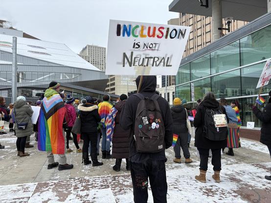 Someone holding a sign saying inclusion is not neutral.
