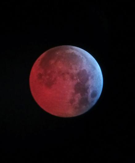 Luna during an eclipse. The left side is a deep orange hue, gradually lightening to a light blue on the right side.