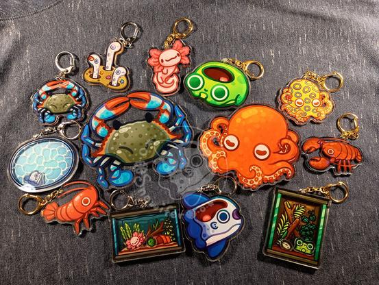 Various acrylic keychains of colorful chibi aquatic creatures including a lobster, garden eel, blue crab, axolotl, an aquarium with an axolotl, a mola with a brain bouncing around, and more.