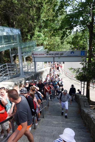 A very long queue several people wide completely fills the long stair entry to the Kasprowy Wierch cable car station. There are at least a hundred people queued, stretching down the street from the bottom of the stairs, and there are more further uphill out of shot.