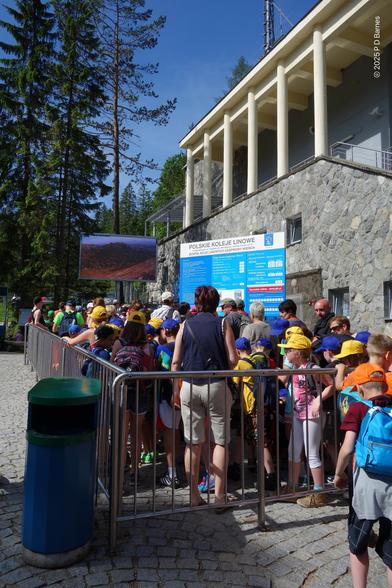The reverse view of the previous shot, showing the queue continuing up the hill to the cable car station, with railed-in pens holding another fifty or sixty people.