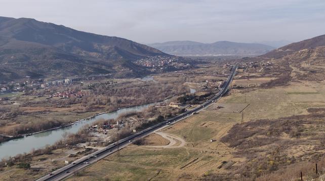 Wide view over a valley with a large river, a motorway, and the mountains in the background.