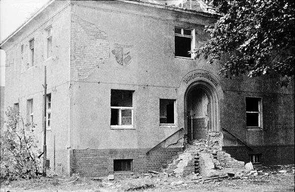 Es ist ein Haus mit herausgerissenen Fenster in zerstörter Eingangstreppe zu sehen.