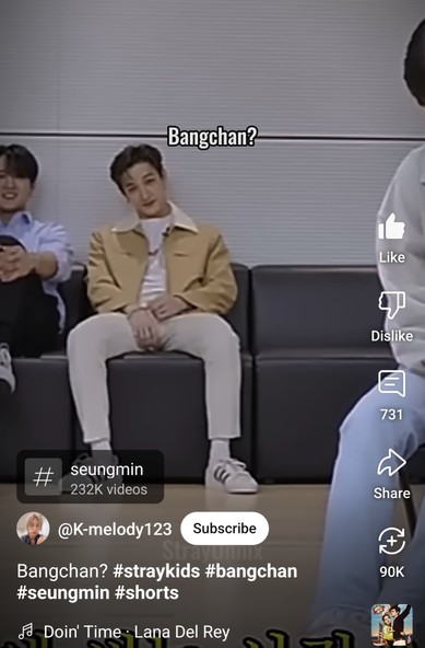 Bang Chan sits on a couch with a predatory look on his face and his hands near his own dick, watching Seungmin who's sitting a little way in front of him and facing the camera. Changbin is partially visible next to Chan, and has a knee pulled up near his chest.