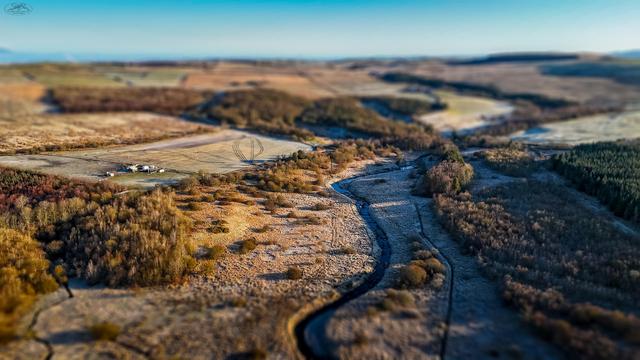 Tilt shift effect on aerial shot over frost covered nature land, woods and river